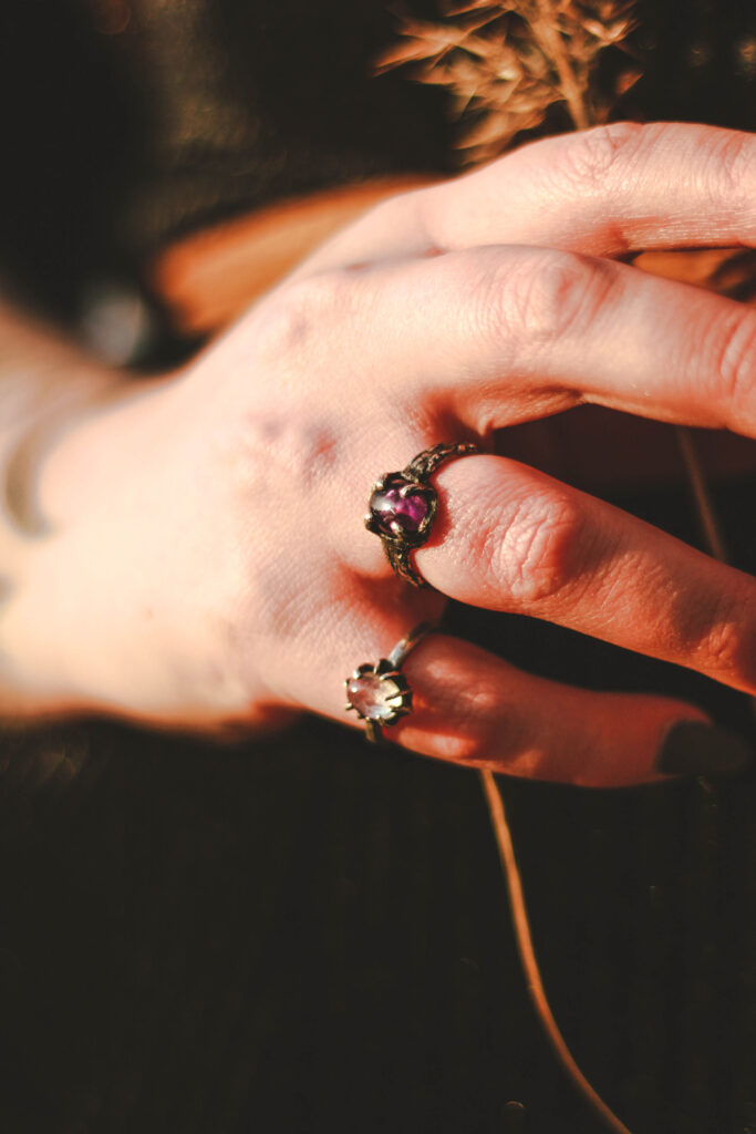 Een hand met twee donkere zilveren ringen om de pink en ringvinger. Eén ring heeft een lichte steen, de ander een paarse.