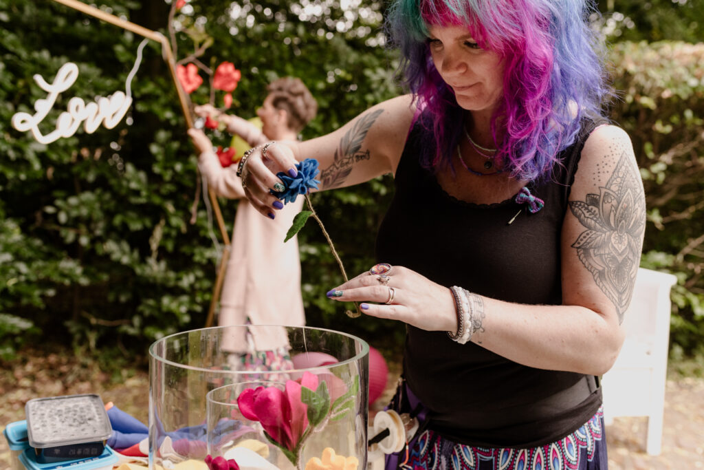 Jolanda stelt een bloemstuk samen met Viltbloemen. In de achtergrond bevestigt Daphne een tak viltbloemen aan de geometrische backdrop met neonbord.