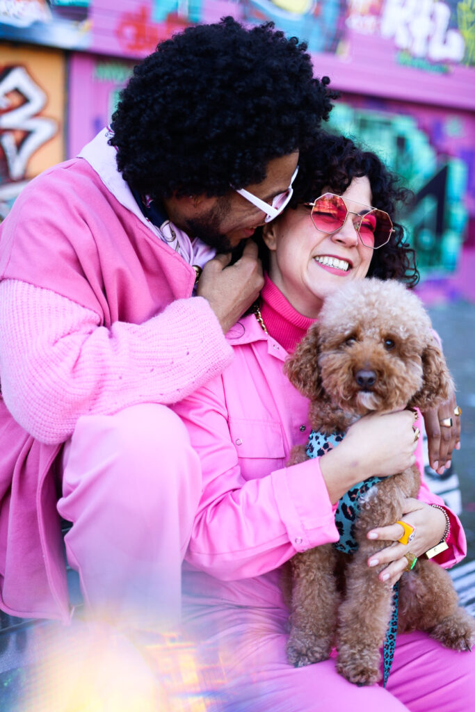 Een koppel in roze outfits zit knus bij elkaar met hun hondje op schoot.